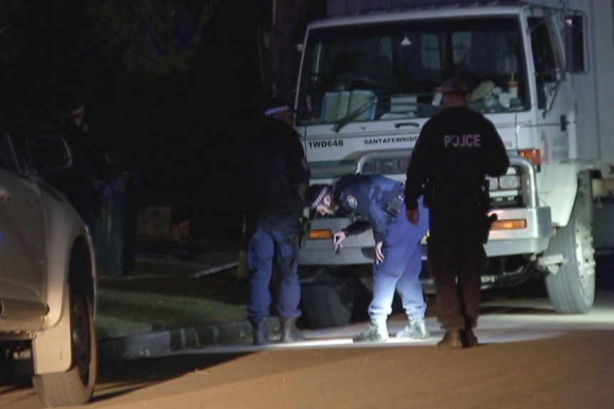 Police using a torch to search in the dark on a road.