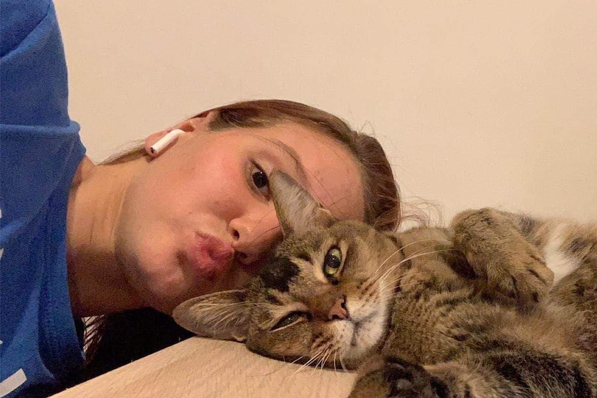 A woman lies on her side and pulls a funny face as she hugs a cat