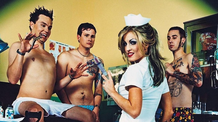actress Janine Lindemulder holds a large needle in front of shirtless members of blink-182 who look scared