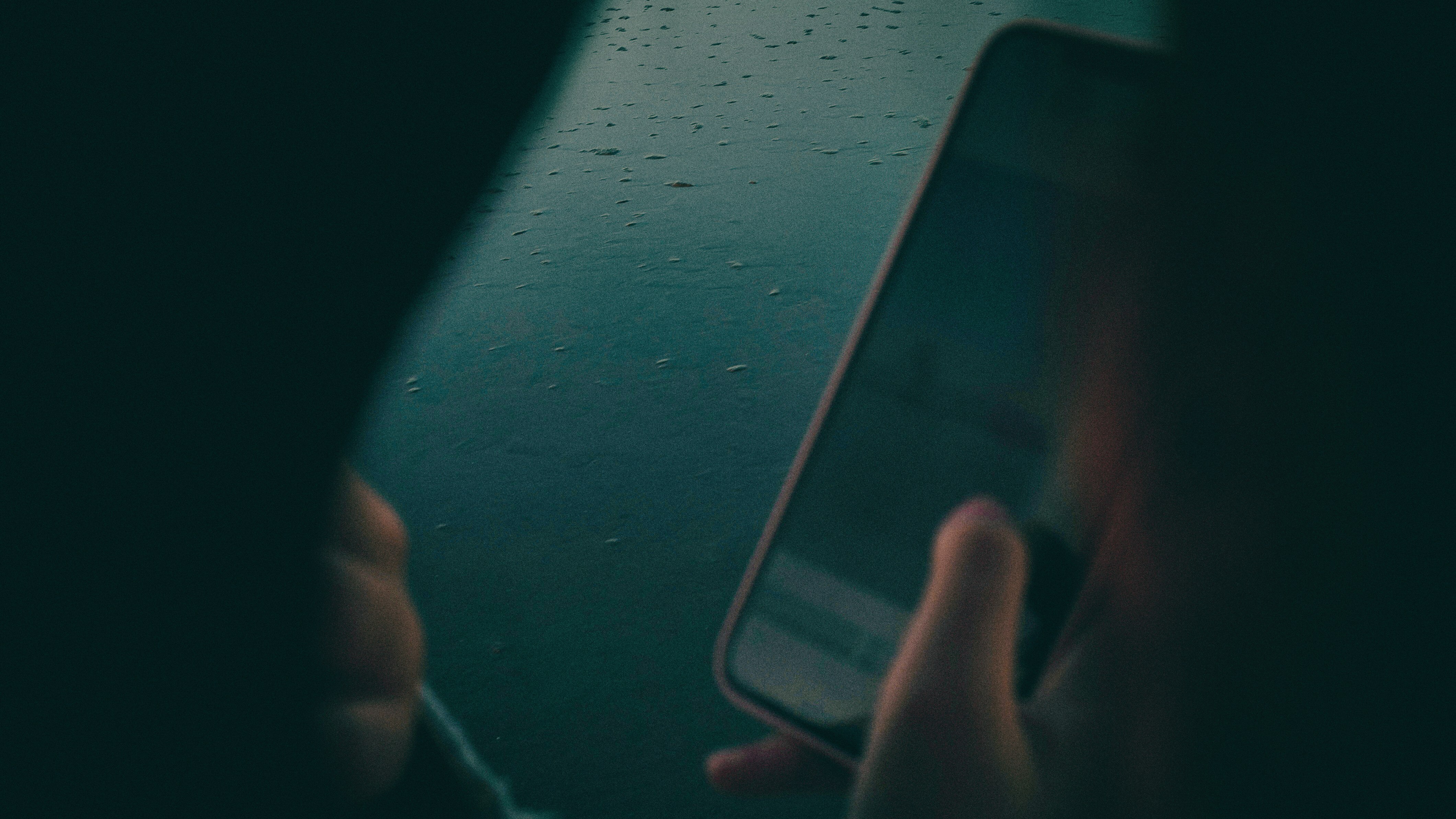 An anonymous male looking at a mobile phone, with a dark background.