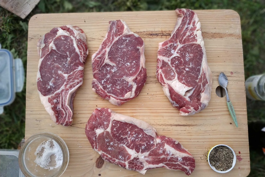 Four raw cuts of steak with salt and pepper on a wooden cutting board to depict best cuts of steak and how to cook them.