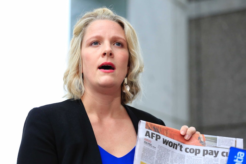Clare O'Neil holds a newspaper reading "AFP won't cop pay cut" as she speaks to reporters