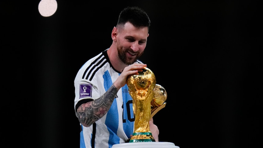 lionel messi smiles at the golden World Cup trophy and touches the top of it