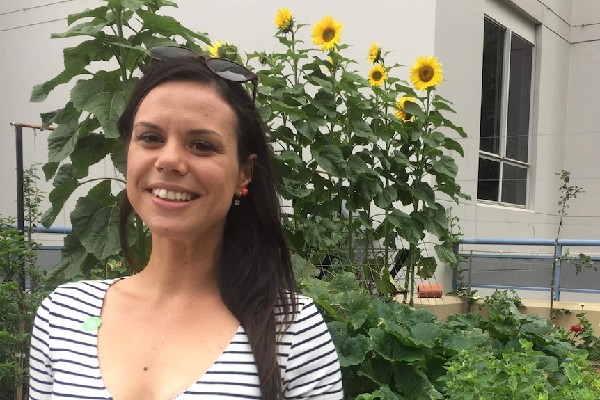 A woman in a horizontal striped shirt in front of sunflowers smiles at the camera. 