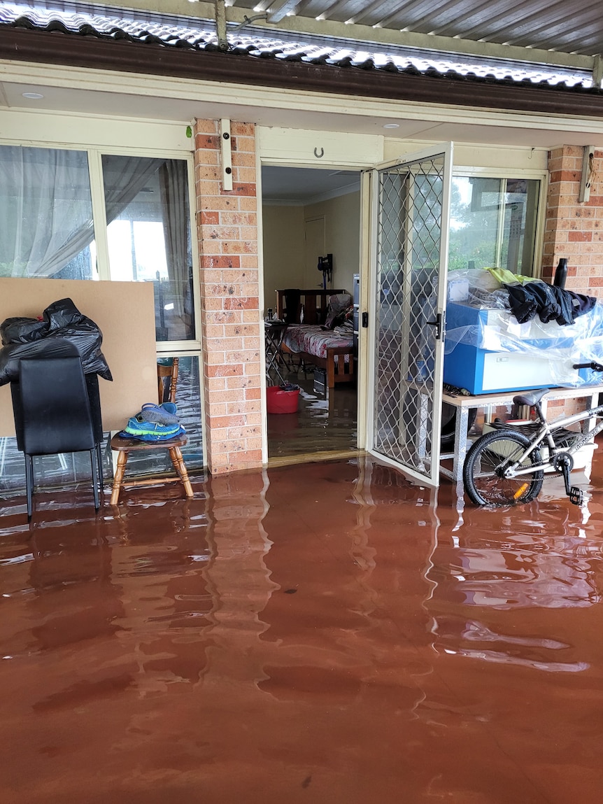 Floodwaters surround a single-storey brick house and creep inside.