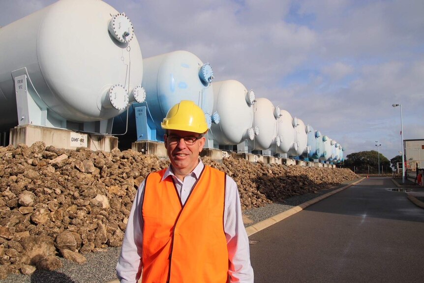 WA Water Minister Dave Kelly stands in front of water tanks wearing a hi-vis vest and hard hat at the Kwinana desalination plant