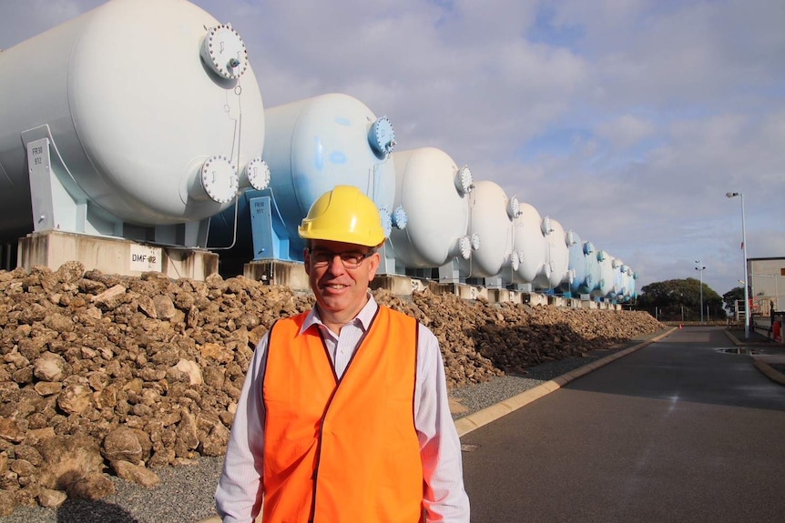 A man wearing a hi-vis vest and hard hat stands in front of a row of water tanks.