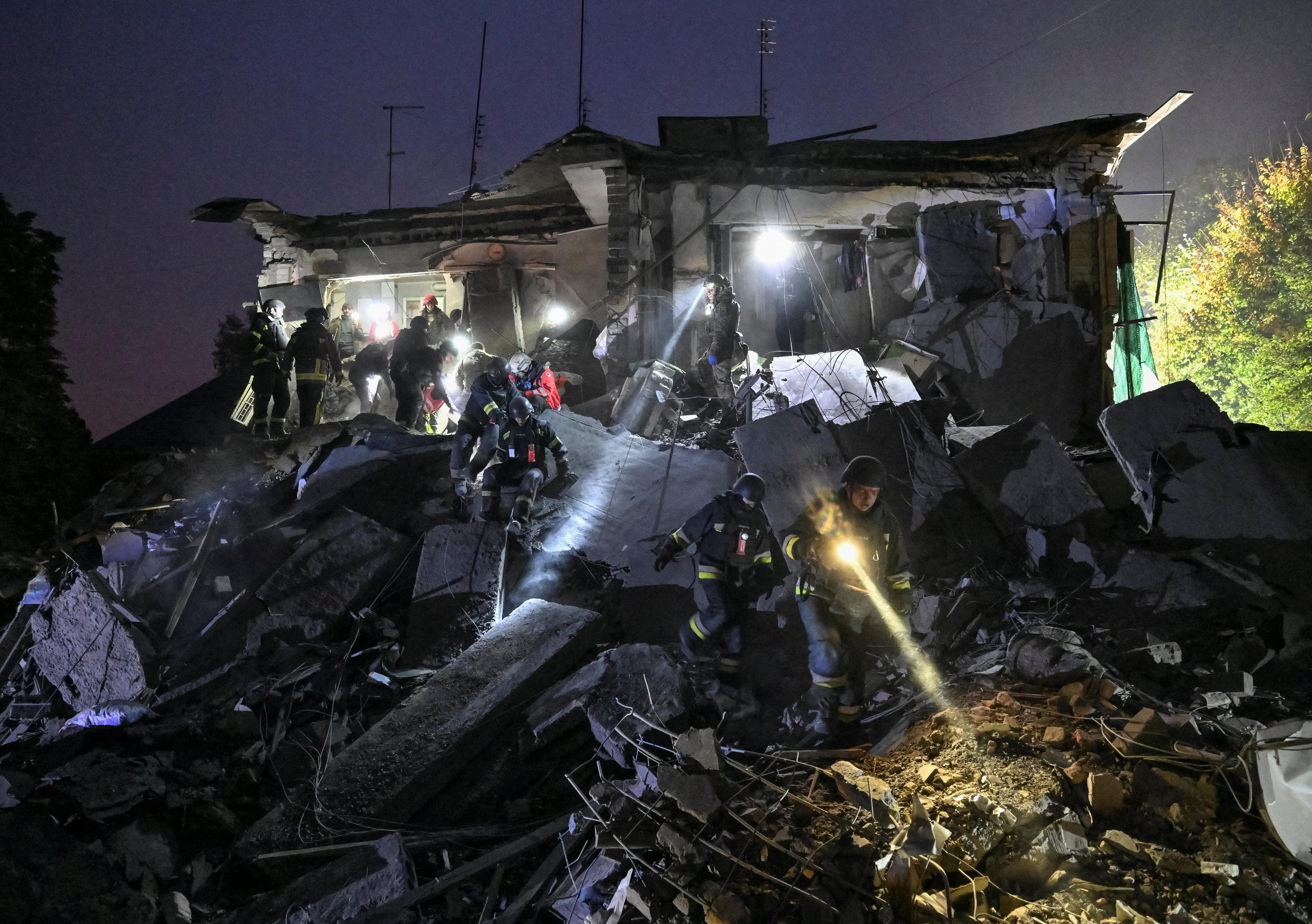 Rescue workers search a building destroyed by air strikes in the dark using torches