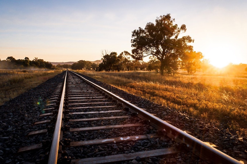 Sunrise over grass fields with train tracks in foreground