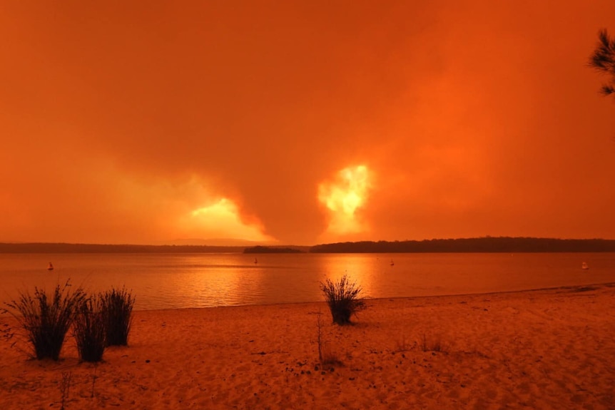 Fires burning on a horizon and reflecting on water and casting orange light over the scene.