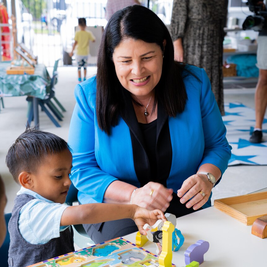 education minister grace grace sits at a kids table playing with blocks and puzzles with a kindergartener smiling