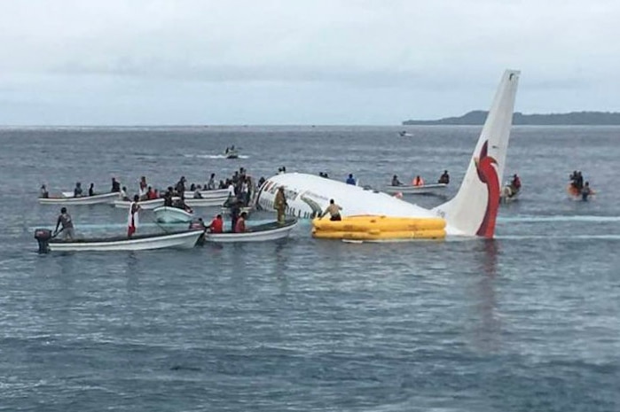 Passengers are disembarking from the submerged plane and boarding boats.