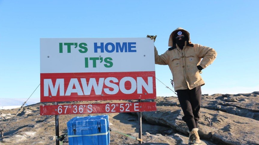 Shane Bilston is rugged up against the cold standing next to the Mawson Base sign