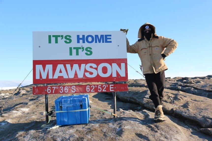 Shane Bilston is rugged up against the cold standing next to the Mawson Base sign