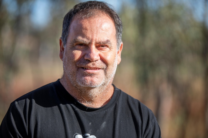 A man in a black tshirt looks directly into the camera.