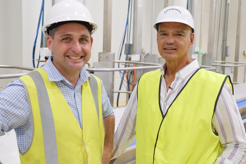 Two men in fluro yellow safety vests and hard hats smile at the camera 