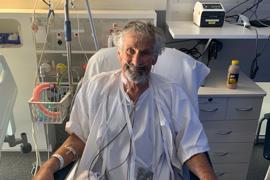 A man sitting up smiling in hospital connected to several intravenous drips and respiratory aids