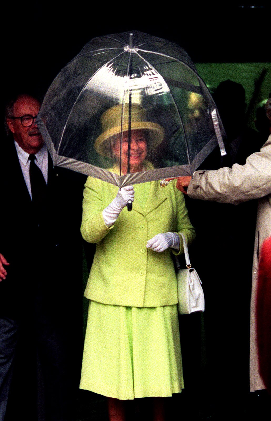 Queen under a clear umbrella, smiling.