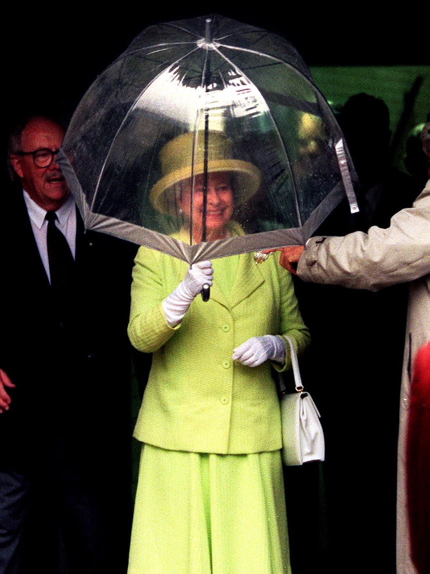 Queen under a clear umbrella, smiling.