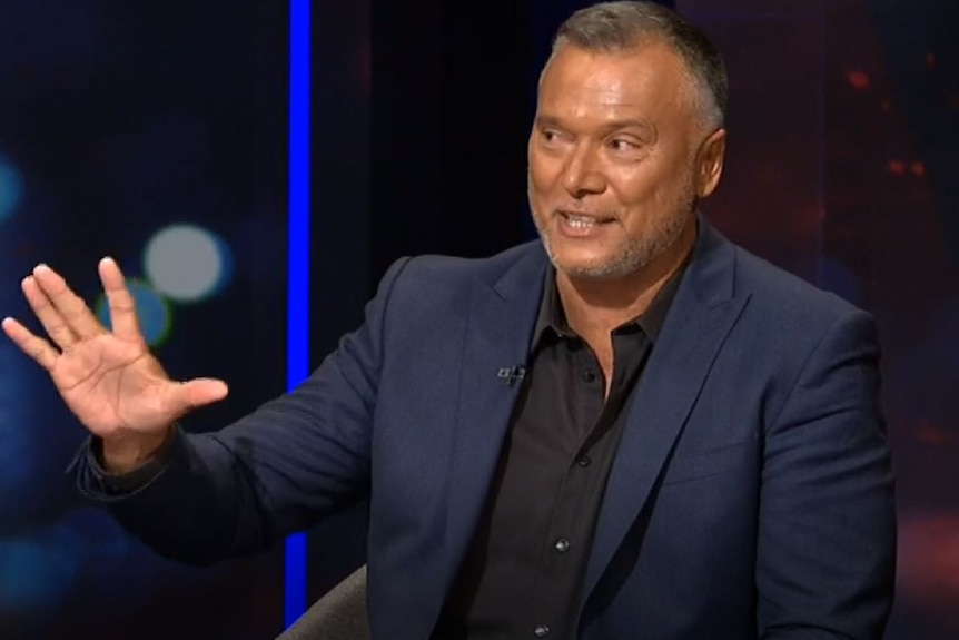 Australian journalist Stan Grant raises his hand to make a point, while half smiling.