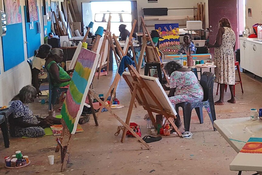 A group of five Indigenous Australian artists work at easels in a room