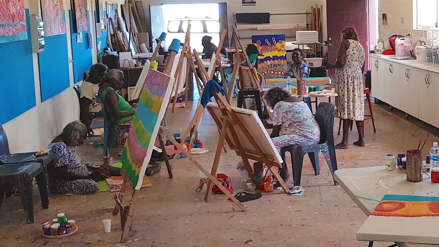 A group of five Indigenous Australian artists work at easels in a room
