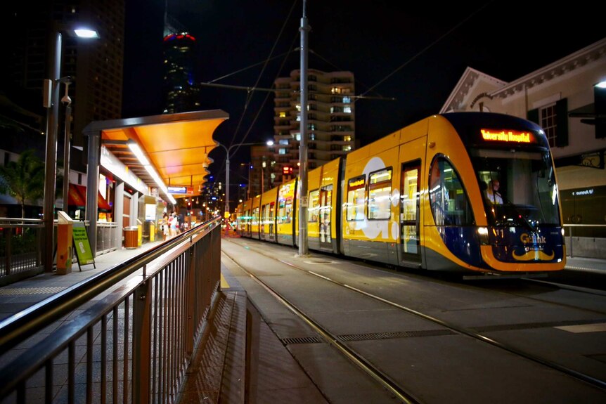 A Gold Coast tram at a tram stop at night.