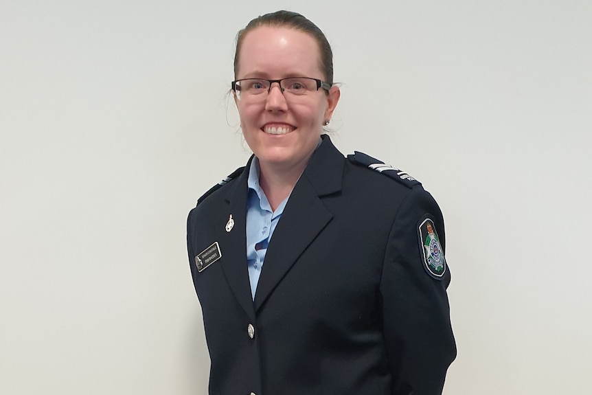 Woman with dark hair, tied back, and glasses, wearing a police uniform, smiling at camera