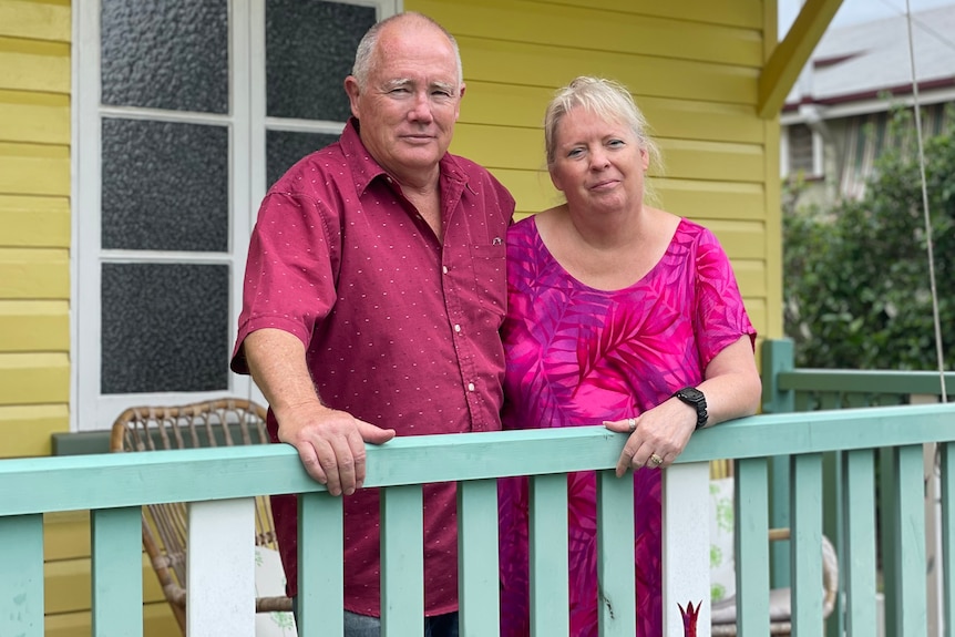 Couple stand on front porch smiling in front of their yellow house