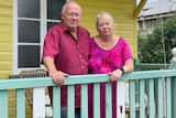 Couple stand on front porch smiling in front of their yellow house