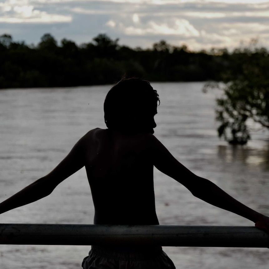 Image of a young boy looking over the Fitzroy River, you can only see his sillhouette.