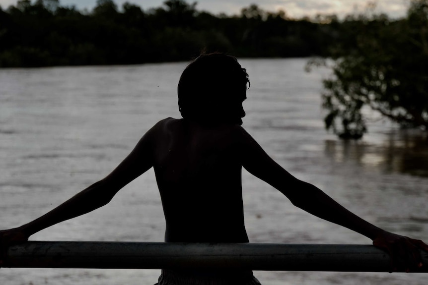 Image of a young boy looking over the Fitzroy River, you can only see his sillhouette.