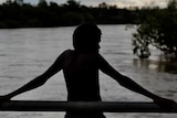 A young boy in silhouette looks over a river in low light.