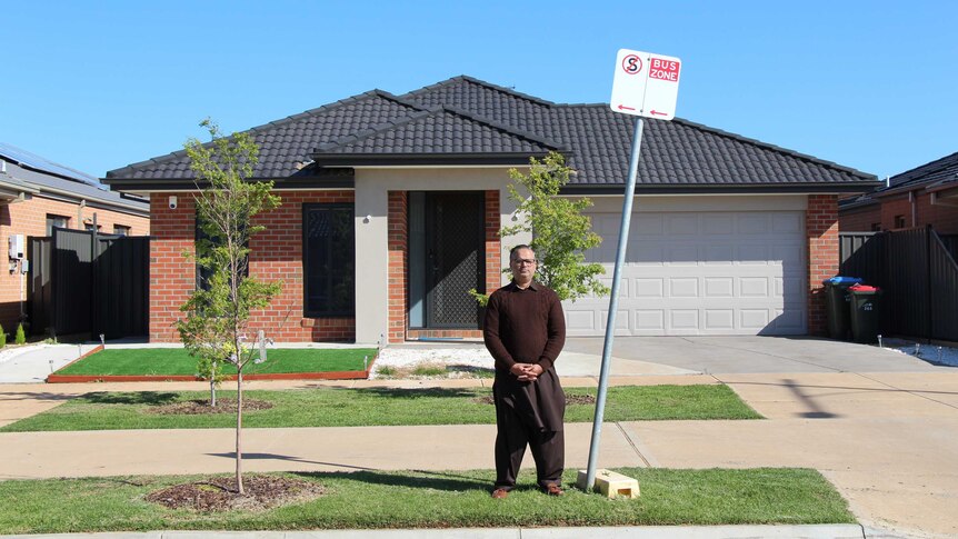 Imran Arshad, in a brown jumper, stands on the footpath near a sign saying 'bus zone' on a sunny day.