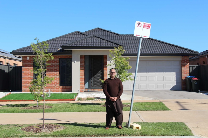 Imran Arshad, in a brown jumper, stands on the footpath near a sign saying 'bus zone' on a sunny day.