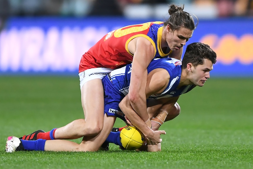 A Brisbane Lions AFL player tackles a North Melbourne opponent on the ground.