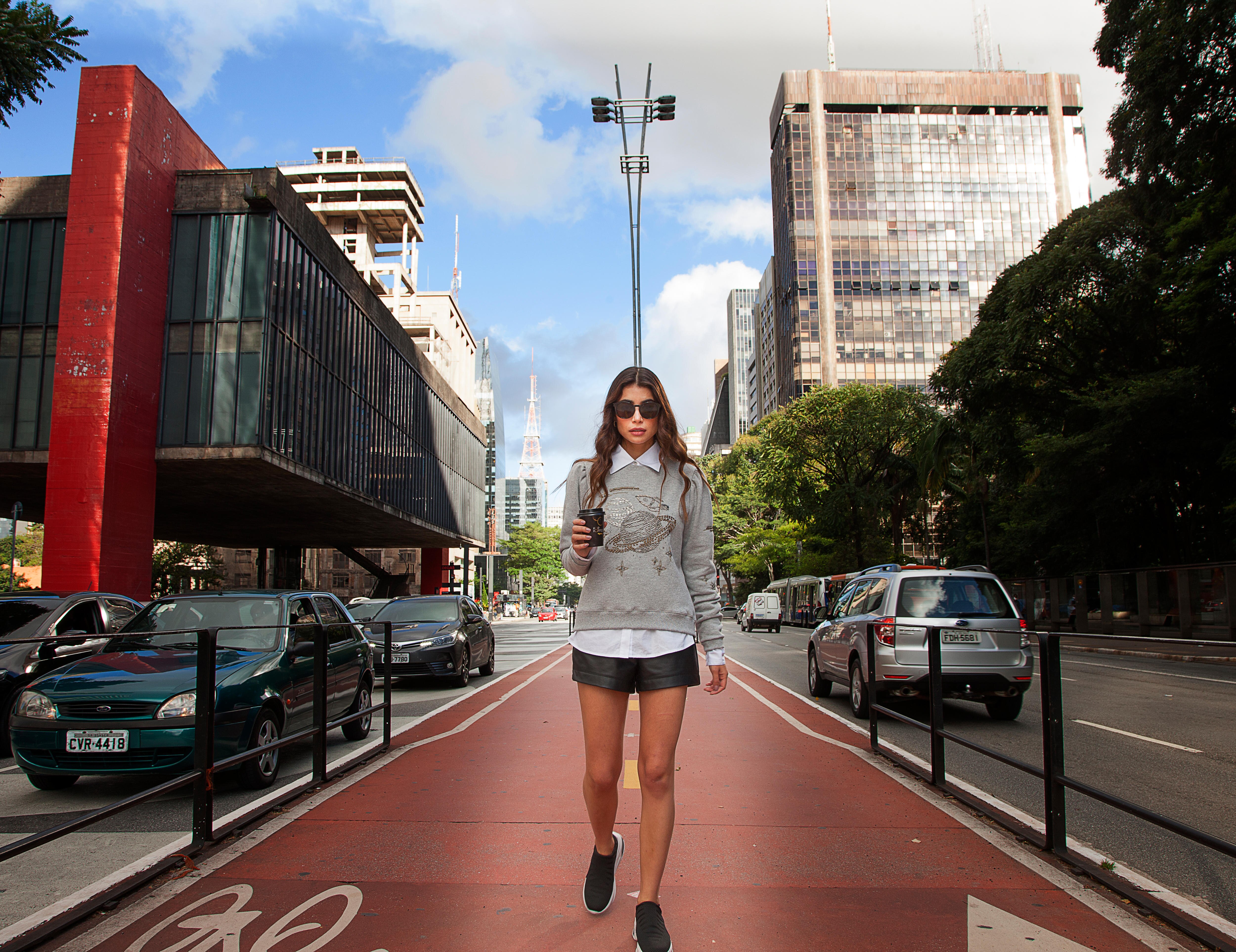A young woman in a grey jumper, white shirt and black skirt walks down a street