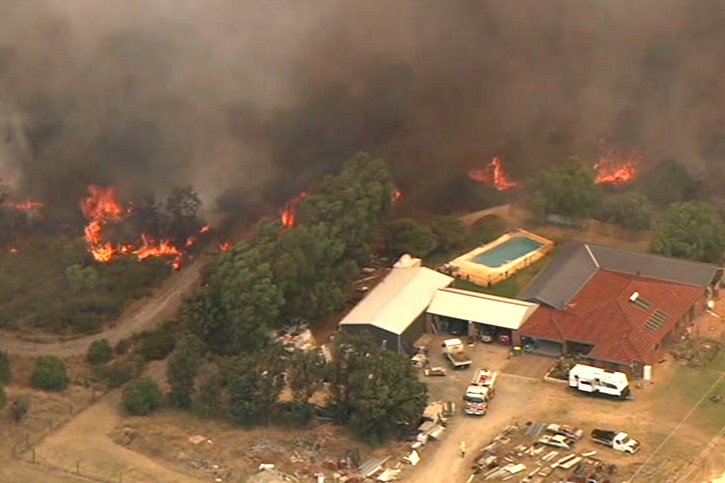 An aerial shot of a fire burning near a property with a pool.