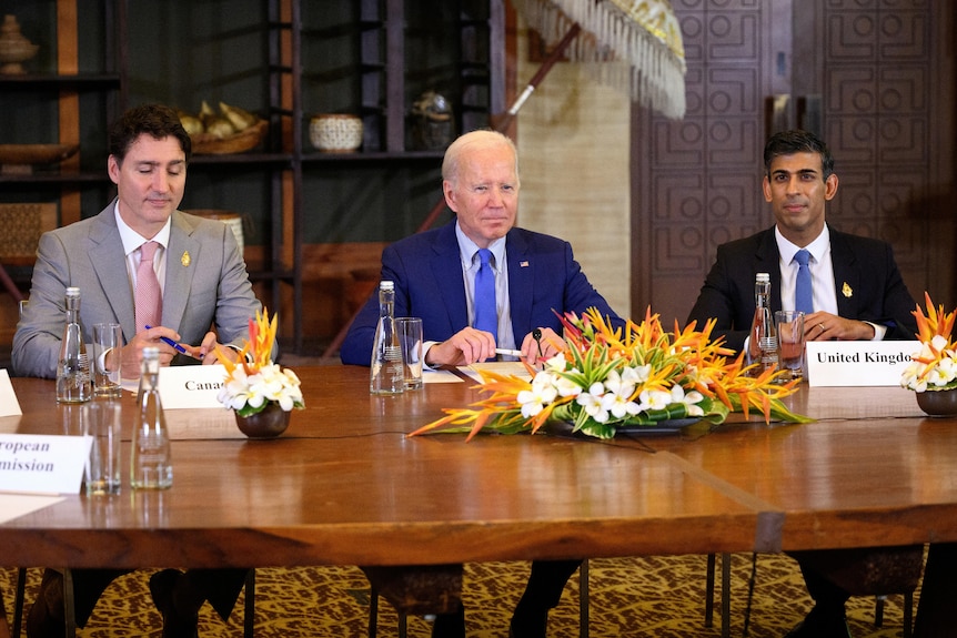 Justin Trudeau, Joe Biden and Rishi Sunak sit at a G20 meeting table. 