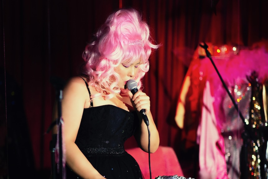 Elly-May singing, wearing a pink wig and leaning on a bedazzled walker.