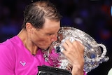 Rafael Nadal hugs and kisses the Australian Open trophy as Daniil Medvedev watches on after their final.