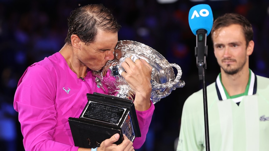 Rafael Nadal hugs and kisses the Australian Open trophy as Daniil Medvedev watches on after their final.