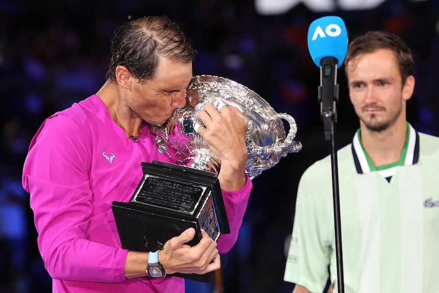 Rafael Nadal hugs and kisses the Australian Open trophy as Daniil Medvedev watches on after their final.