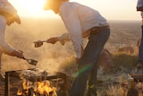 Two cowboys in the outback standing over a campfire
