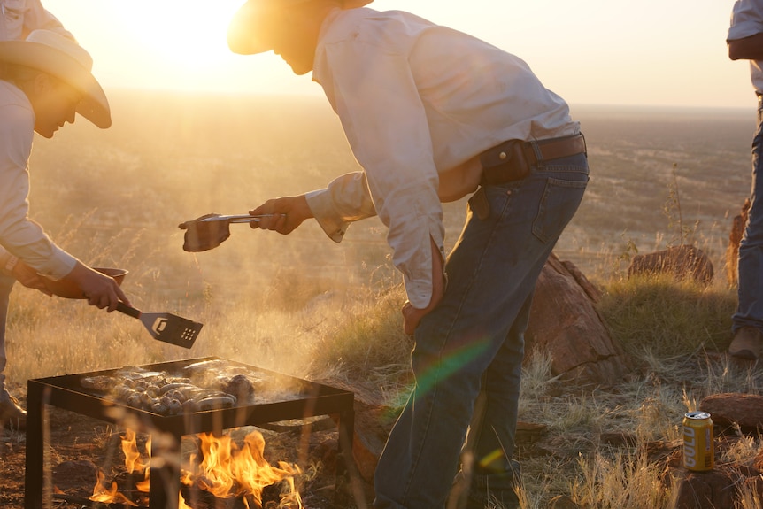 Two cowboys in the outback standing over a campfire