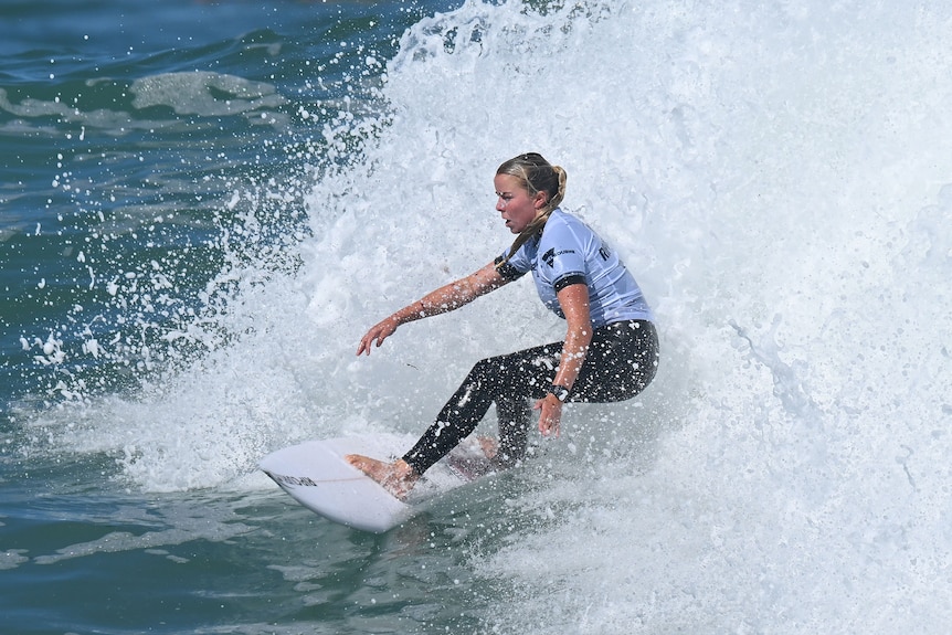 An Australian surfer bends her body to turn her board as she moves through the water during a competition.