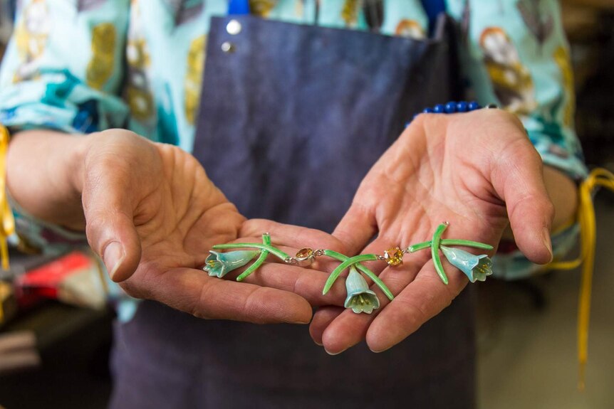 Woman's hands holding three enamelled flowers and stamens with connecting gemstones.