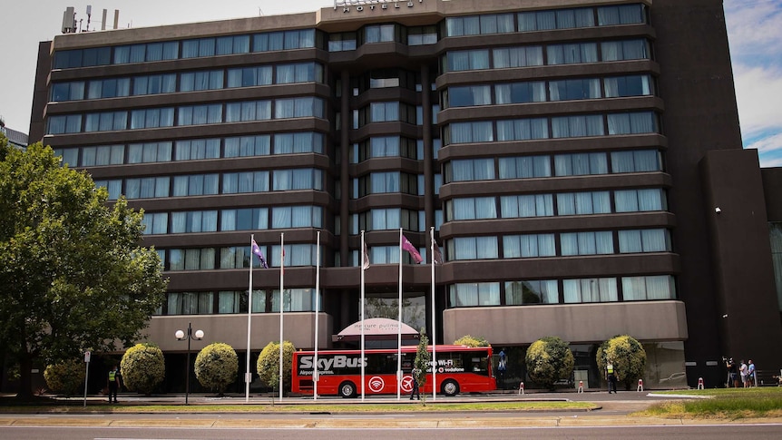 A red Skybus parked outside a multi-storey hotel.