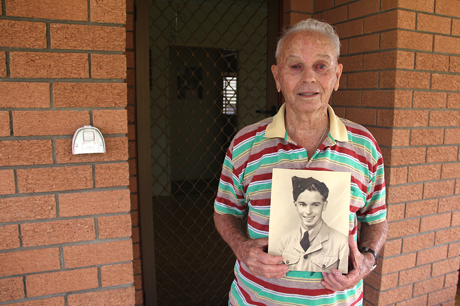 A elderly man holds an unframed black and white portrait of himself in RAAF uniform.