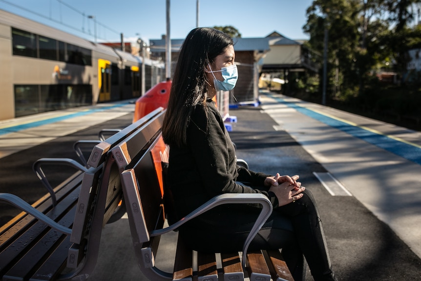 a woman wearing a mask sitting at a train station